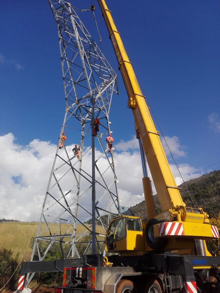 Operai su traliccio elettrico con gru gialla.