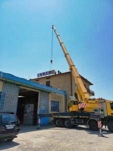 Gru con braccio solleva insegna su edificio industriale.