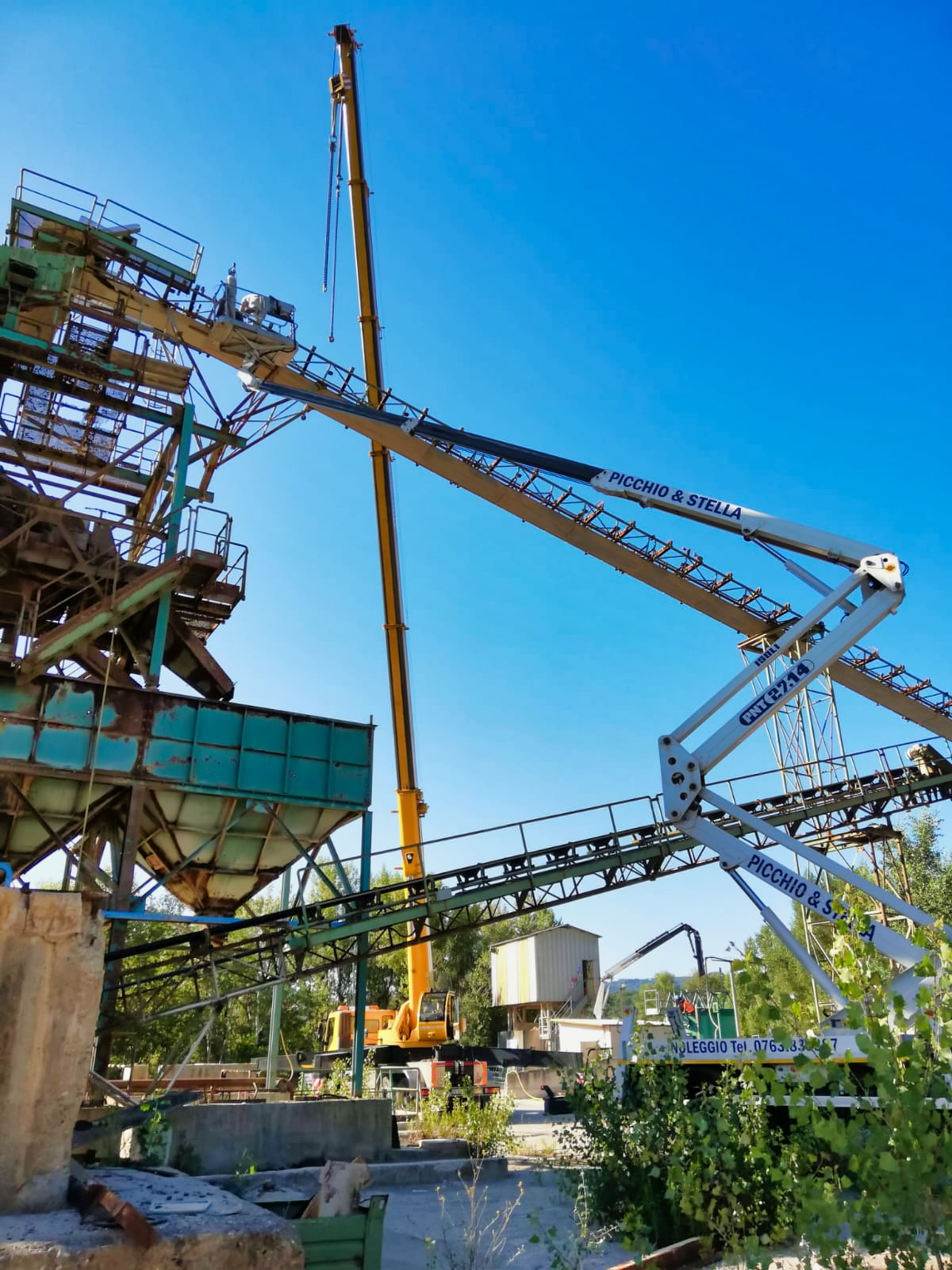 Cantiere con gru e strutture metalliche sotto cielo azzurro.