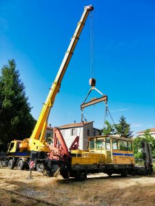 Gru gialla solleva veicolo su sfondo di case.