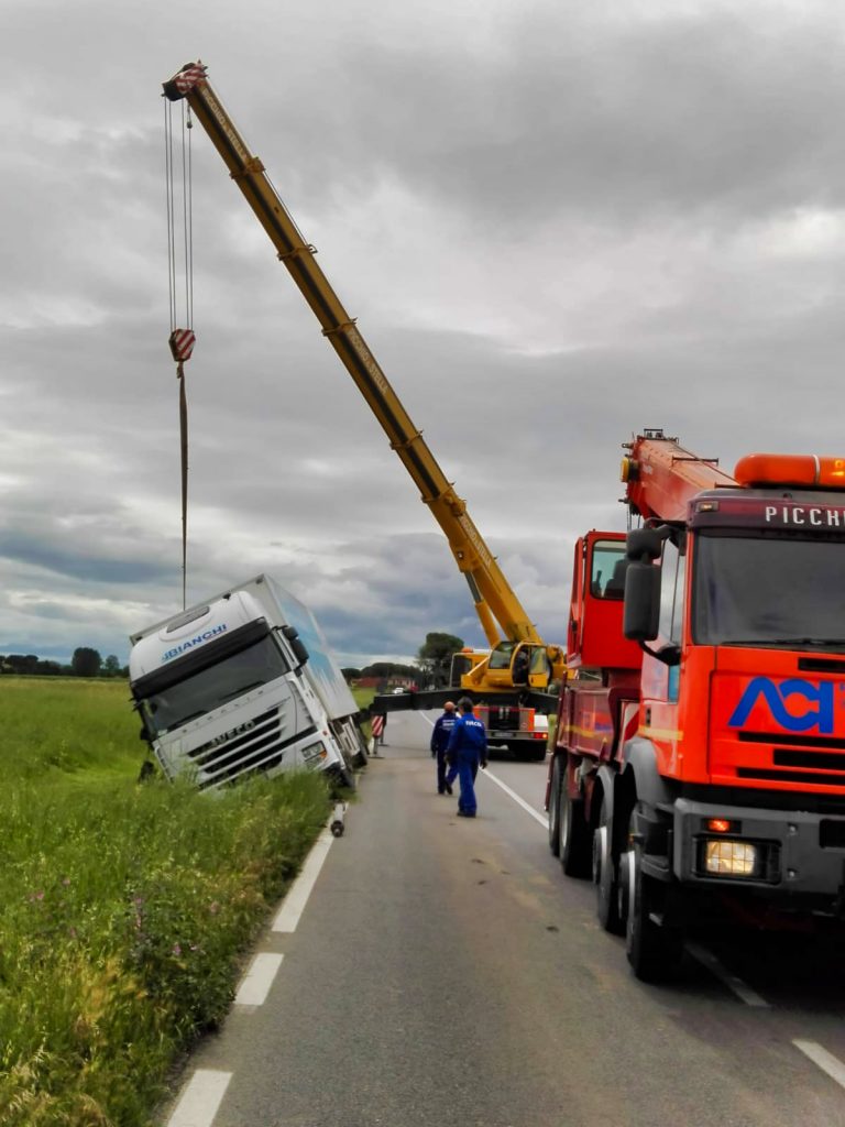 Camion ribaltato su strada, gru in azione per recupero.