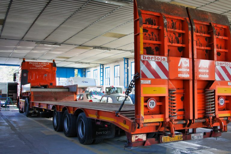 Camion arancione in un'officina con rimorchio.