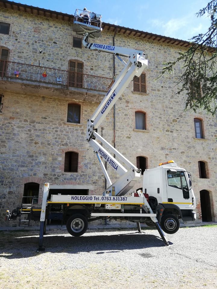Camion con piattaforma elevatrice davanti a edificio in pietra.